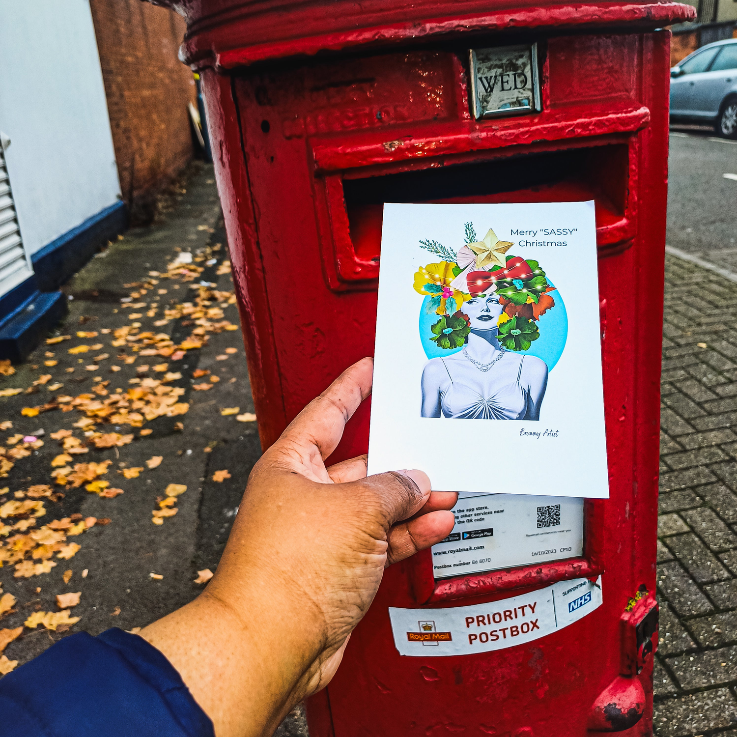 Person holding a Christmas card with a festive design in front of a lit Christmas tree.