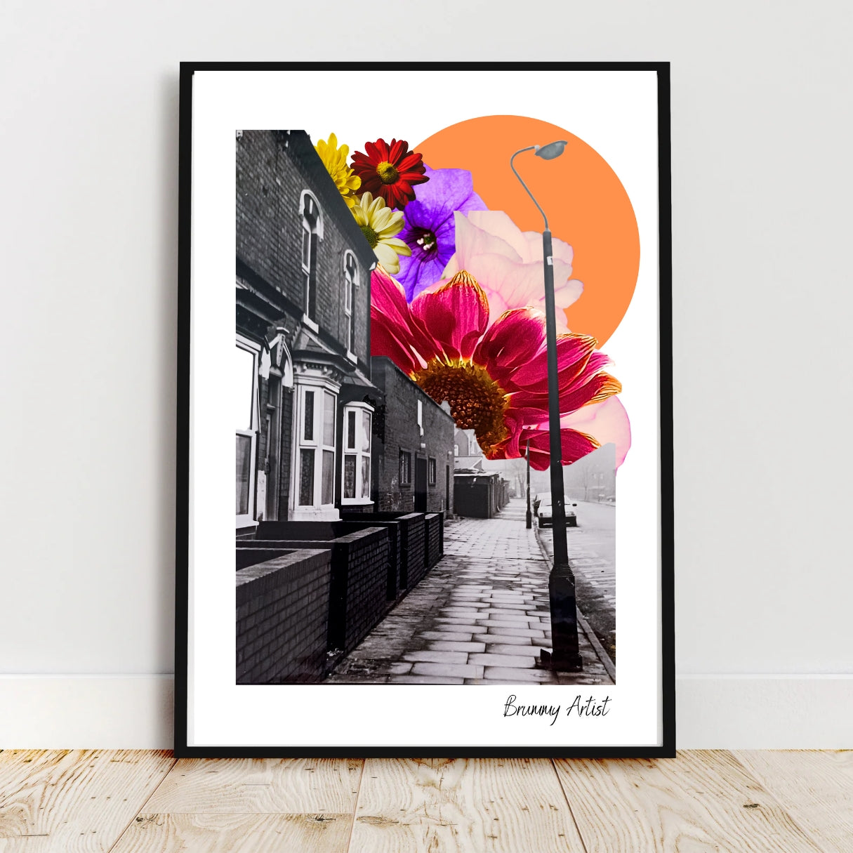 Framed artwork of a black-and-white street with colorful flowers and an orange circle in the background.