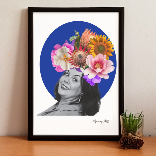 The "Portrait commission floral collage" by The Brummy Artist UK features a framed artwork of a smiling woman in black and white, accented with a vibrant custom floral collage on her head, set against a blue circle, and elegantly displayed on a wooden surface alongside a small potted plant.